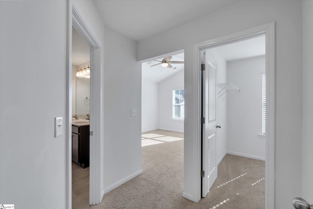 hall with sink, light colored carpet, and vaulted ceiling