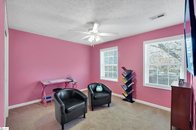 sitting room featuring a textured ceiling, ceiling fan, a healthy amount of sunlight, and light carpet