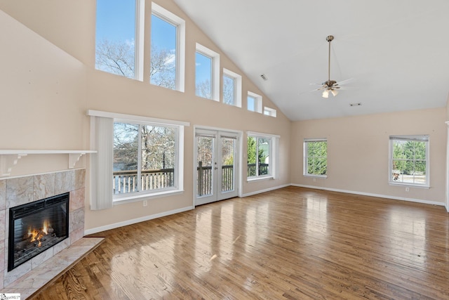 unfurnished living room featuring hardwood / wood-style flooring, ceiling fan, a towering ceiling, and a tile fireplace