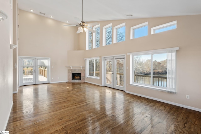 unfurnished living room featuring french doors, a towering ceiling, ceiling fan, dark wood-type flooring, and a tile fireplace