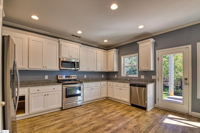 kitchen with white cabinets, light wood-type flooring, stainless steel appliances, and dark stone counters