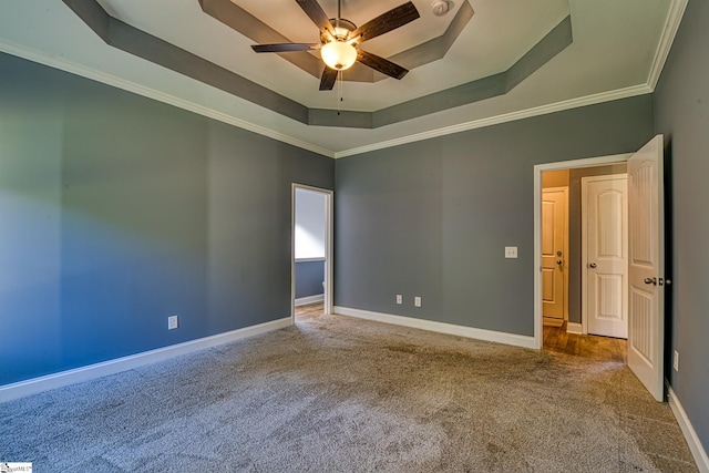 empty room with a raised ceiling, ceiling fan, crown molding, and carpet floors