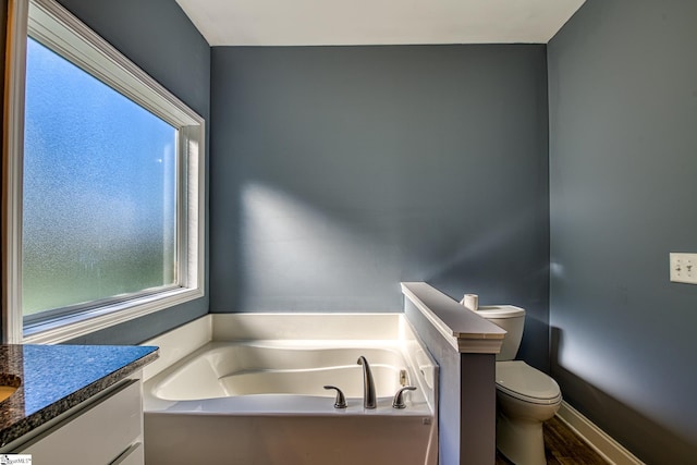 bathroom featuring vanity, a tub to relax in, and toilet