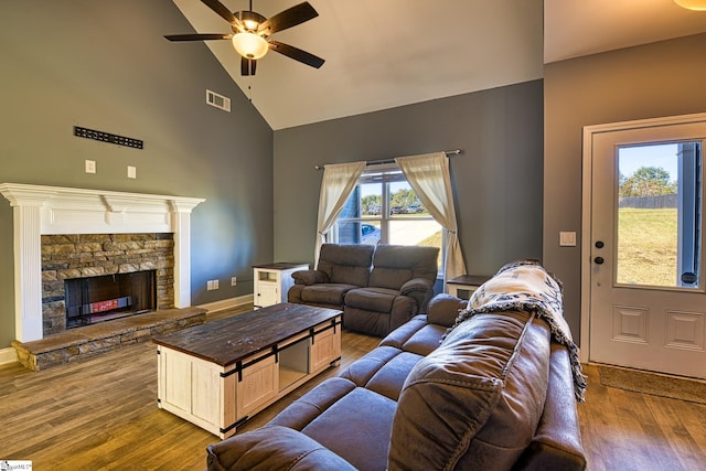 living room featuring high vaulted ceiling, light hardwood / wood-style flooring, a stone fireplace, and ceiling fan