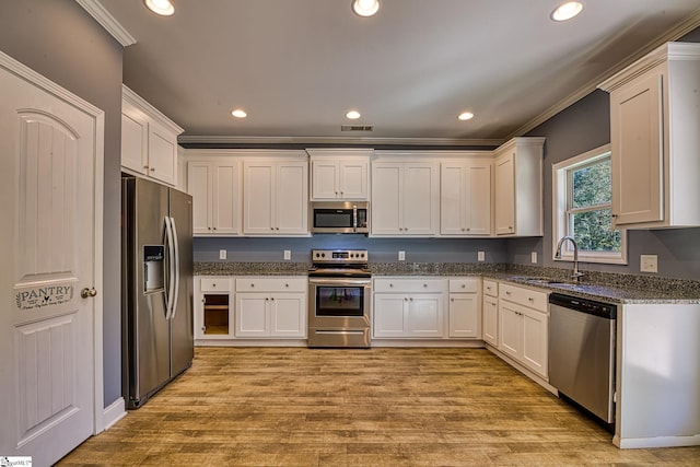 kitchen featuring light wood-type flooring, dark stone counters, stainless steel appliances, sink, and white cabinetry