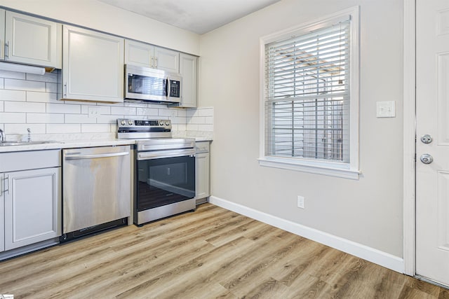 kitchen with sink, decorative backsplash, gray cabinets, appliances with stainless steel finishes, and light hardwood / wood-style floors