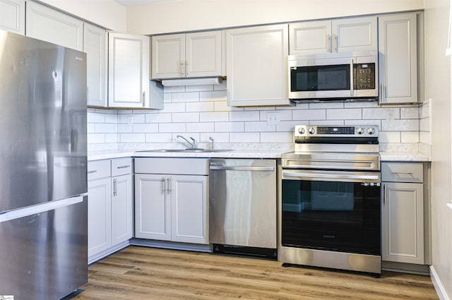 kitchen with gray cabinetry, sink, tasteful backsplash, appliances with stainless steel finishes, and light wood-type flooring