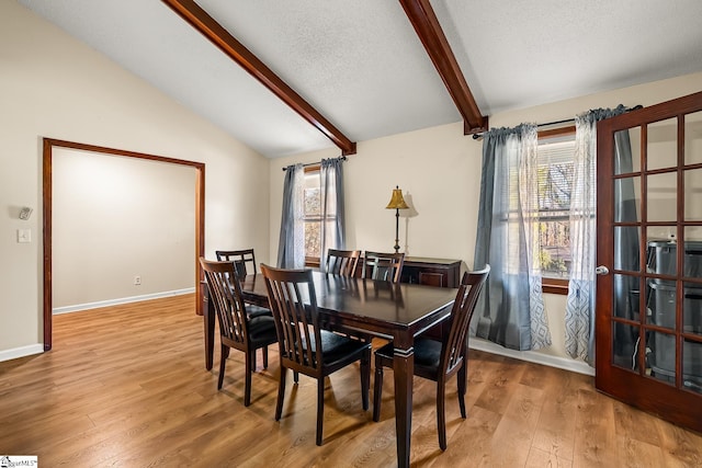 dining room featuring vaulted ceiling with beams, light hardwood / wood-style floors, and a textured ceiling