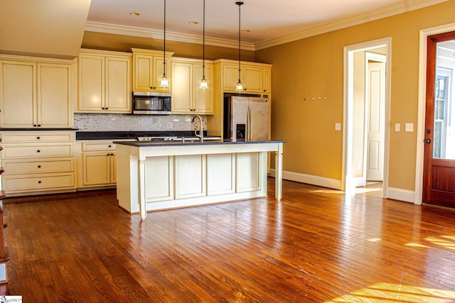 kitchen featuring backsplash, cream cabinets, pendant lighting, a kitchen island with sink, and appliances with stainless steel finishes