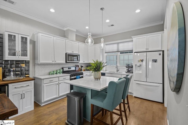 kitchen featuring hanging light fixtures, sink, appliances with stainless steel finishes, white cabinetry, and a breakfast bar area