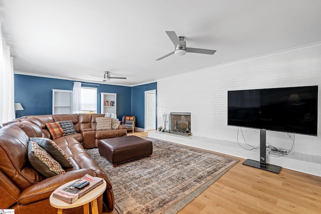 living room with wood-type flooring, a large fireplace, ceiling fan, and ornamental molding