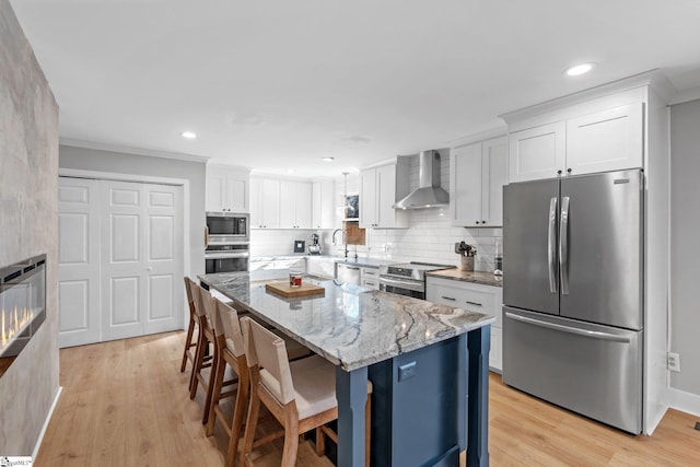 kitchen with a kitchen breakfast bar, wall chimney exhaust hood, stainless steel appliances, a center island, and white cabinetry