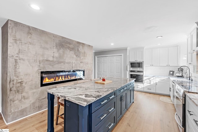 kitchen with white cabinetry, a large fireplace, a center island, light hardwood / wood-style flooring, and appliances with stainless steel finishes