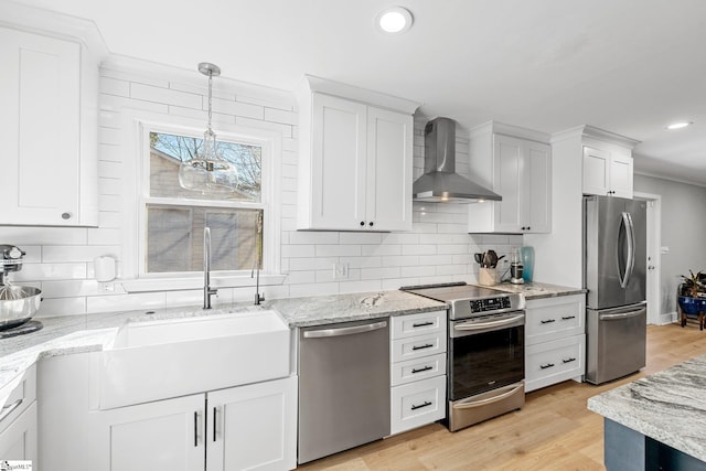 kitchen with appliances with stainless steel finishes, sink, white cabinetry, and wall chimney range hood