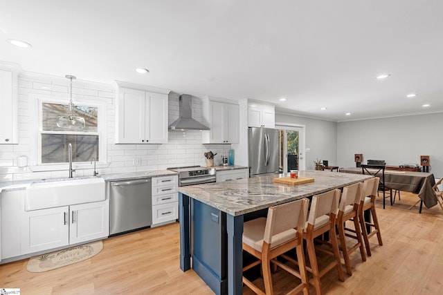 kitchen with a center island, wall chimney exhaust hood, pendant lighting, white cabinets, and appliances with stainless steel finishes