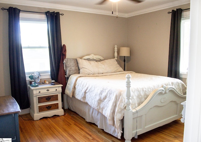 bedroom featuring ceiling fan, light hardwood / wood-style floors, ornamental molding, and multiple windows