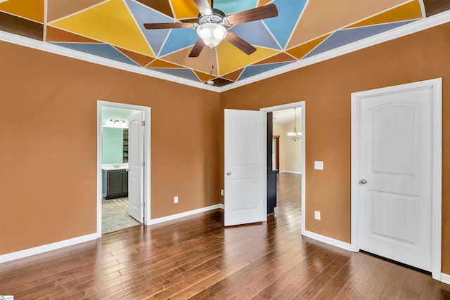 unfurnished bedroom featuring ensuite bathroom, ceiling fan with notable chandelier, hardwood / wood-style flooring, and ornamental molding