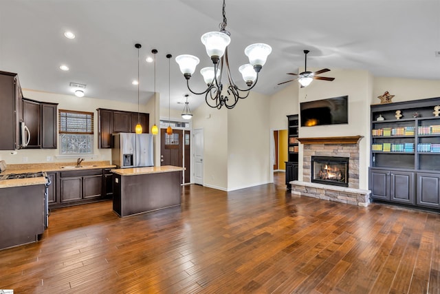 kitchen featuring appliances with stainless steel finishes, light stone counters, a center island, a stone fireplace, and hanging light fixtures