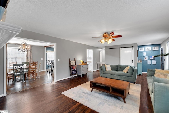 living room featuring a textured ceiling, a barn door, ceiling fan with notable chandelier, and dark hardwood / wood-style floors