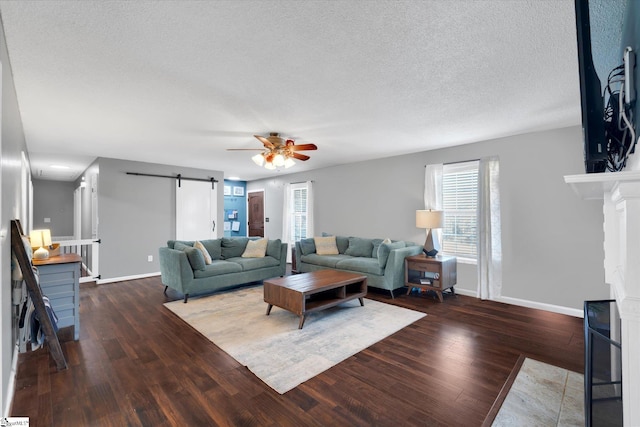 living room featuring a textured ceiling, a barn door, ceiling fan, and dark hardwood / wood-style floors