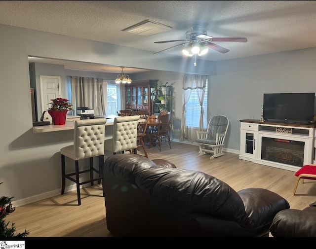 living room with light wood-type flooring, a textured ceiling, and ceiling fan with notable chandelier