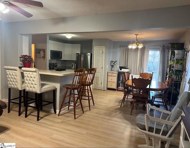 kitchen with hanging light fixtures, a breakfast bar area, white cabinets, black appliances, and ceiling fan with notable chandelier