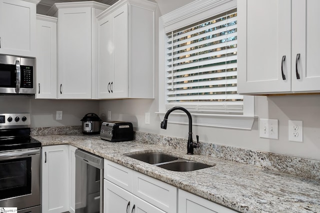 kitchen featuring white cabinets, stainless steel appliances, light stone counters, and sink