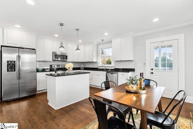 kitchen with dark wood-type flooring, hanging light fixtures, a kitchen island, white cabinetry, and stainless steel appliances