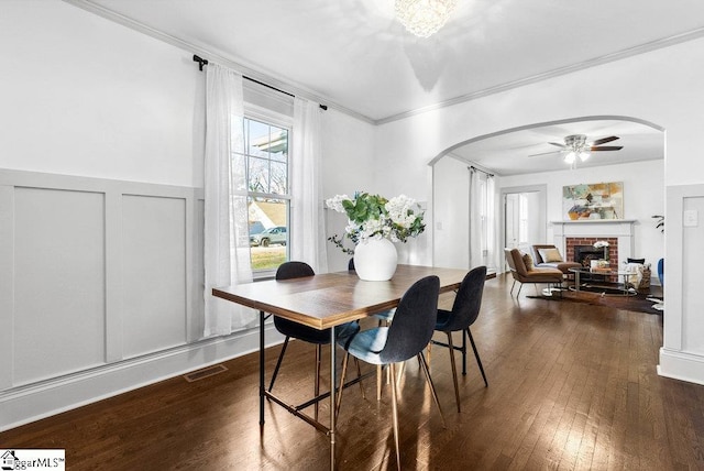 dining space with crown molding, a fireplace, ceiling fan, and dark wood-type flooring