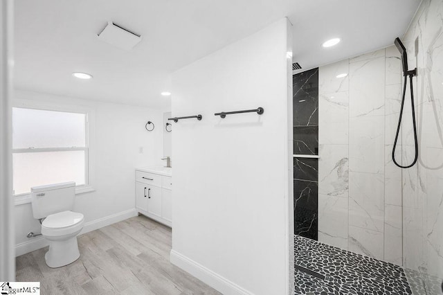 bathroom with hardwood / wood-style floors, vanity, a tile shower, and toilet