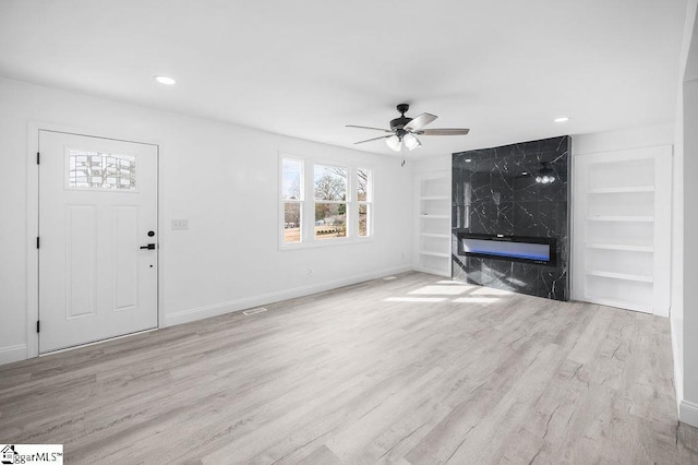 unfurnished living room featuring a fireplace, light hardwood / wood-style flooring, built in features, and ceiling fan