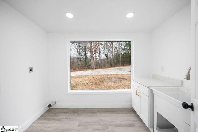 clothes washing area with hookup for an electric dryer, light wood-type flooring, and cabinets