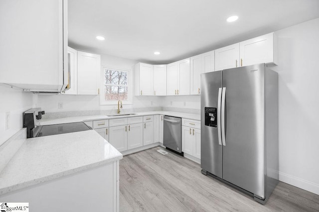 kitchen with appliances with stainless steel finishes, light wood-type flooring, light stone counters, sink, and white cabinetry