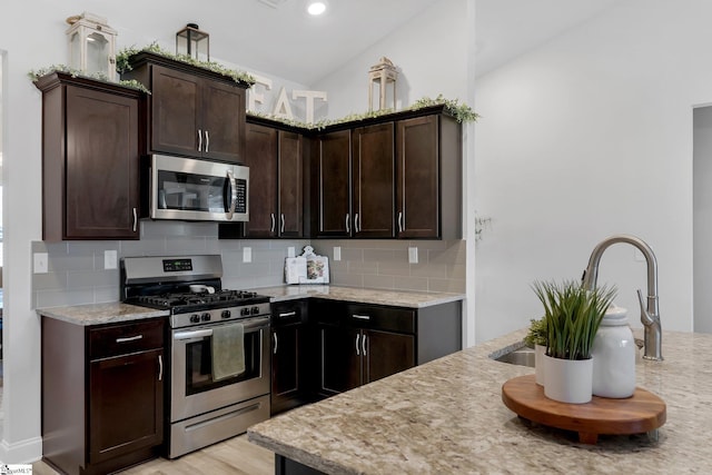 kitchen with appliances with stainless steel finishes, tasteful backsplash, light stone counters, and dark brown cabinets