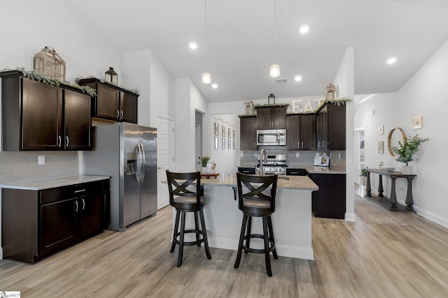 kitchen featuring backsplash, dark brown cabinetry, a kitchen island with sink, and appliances with stainless steel finishes