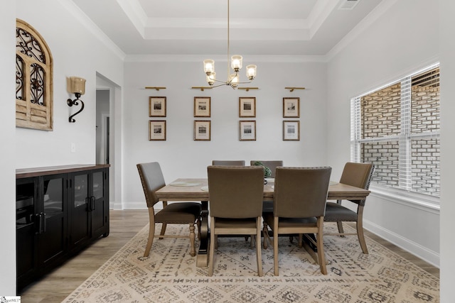 dining space featuring a tray ceiling, crown molding, a chandelier, and light wood-type flooring