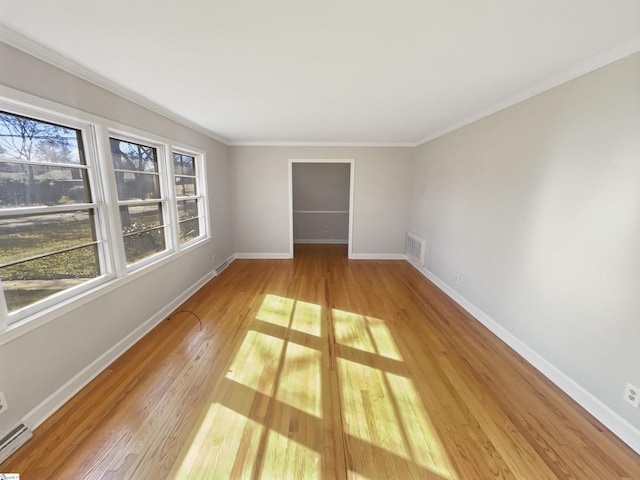 empty room with ornamental molding, hardwood / wood-style flooring, baseboard heating, and a healthy amount of sunlight