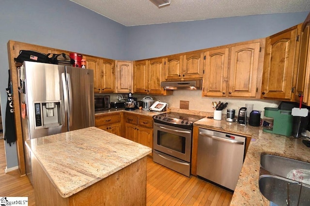 kitchen with light stone countertops, sink, stainless steel appliances, light hardwood / wood-style flooring, and a textured ceiling