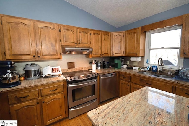 kitchen with appliances with stainless steel finishes, light wood-type flooring, a textured ceiling, vaulted ceiling, and sink