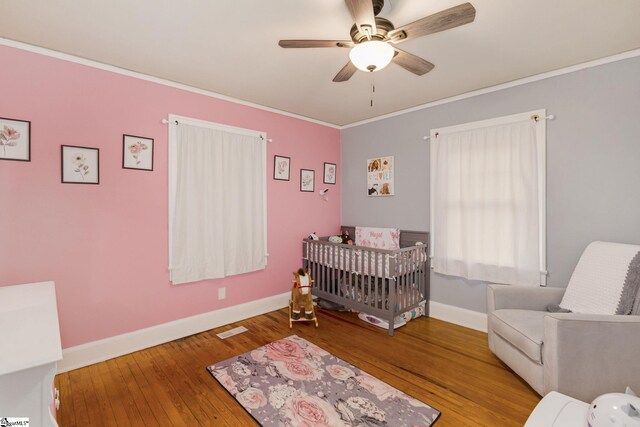 bedroom featuring ceiling fan, hardwood / wood-style floors, a crib, and ornamental molding