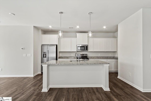 kitchen featuring light stone countertops, white cabinetry, stainless steel appliances, pendant lighting, and a center island with sink