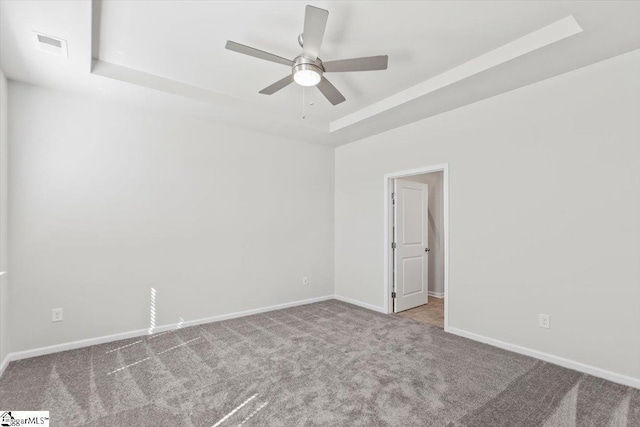 spare room with ceiling fan, a raised ceiling, and light colored carpet