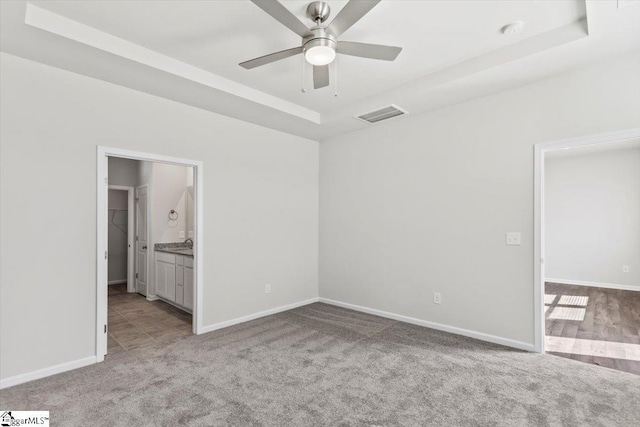 unfurnished bedroom with light carpet, a raised ceiling, ceiling fan, a spacious closet, and connected bathroom