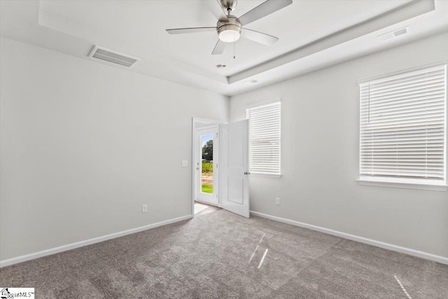 carpeted spare room featuring a tray ceiling and ceiling fan