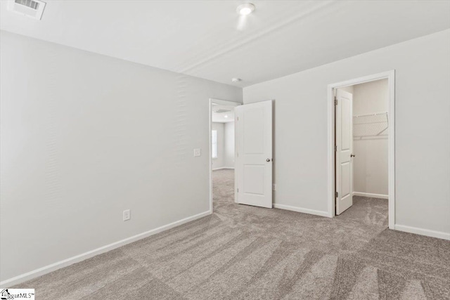 unfurnished bedroom with a walk in closet, a closet, and light colored carpet