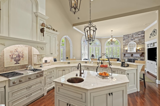 kitchen featuring stainless steel gas stovetop, a kitchen island with sink, hanging light fixtures, light stone counters, and kitchen peninsula