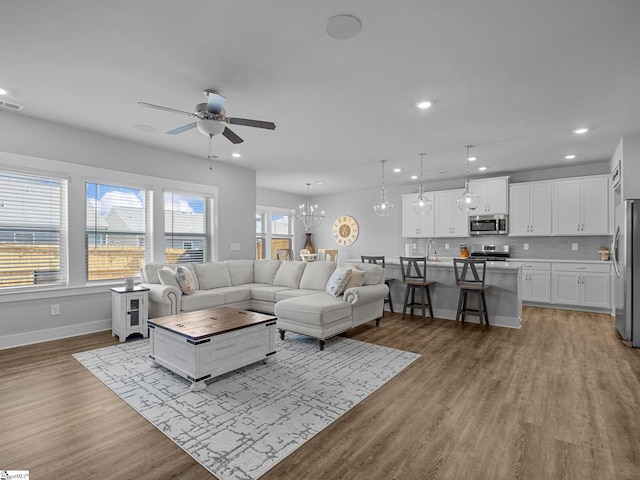 living room with ceiling fan with notable chandelier, sink, and light hardwood / wood-style flooring