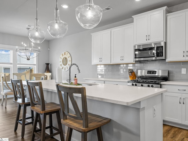 kitchen featuring a center island with sink, white cabinets, appliances with stainless steel finishes, and tasteful backsplash