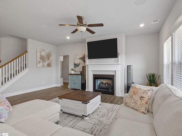 living room with ceiling fan, wood-type flooring, and a tile fireplace