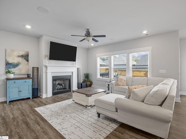 living room with hardwood / wood-style flooring, ceiling fan, and a tiled fireplace